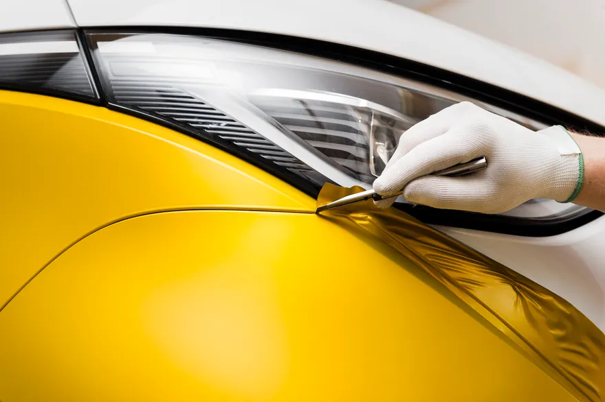 Detalj, skalpell mot folie på bil. Gul folie